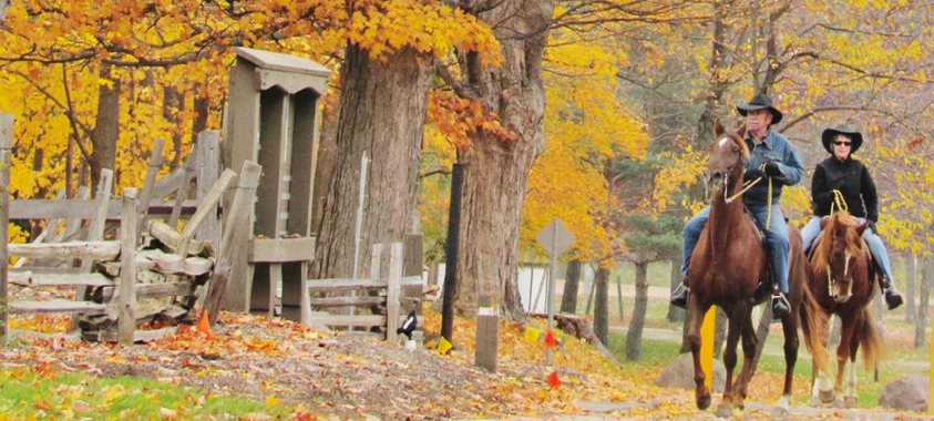 Two people riding horses in the fall at Addison Oaks