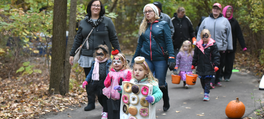 Smiling children wearing halloween costumes walk along a trail in the park during the fall