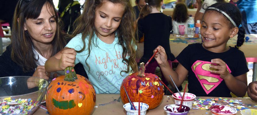 Two smiling children decorate a Halloween pumpkin