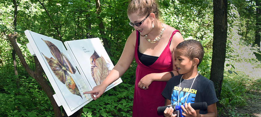 A person points to an educational marker along the trail while a child looks on