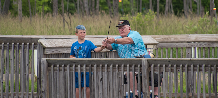An older adult helps a child with his fishing rod at Independence Oaks North