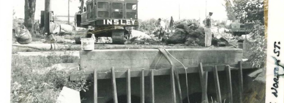 Historic photo of excavator and man above a drainage system