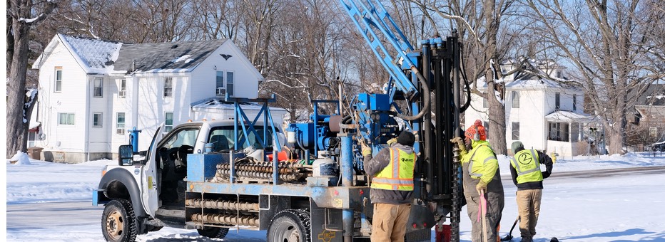 Three workers inspecting specialized equipment on back of truck in residential area